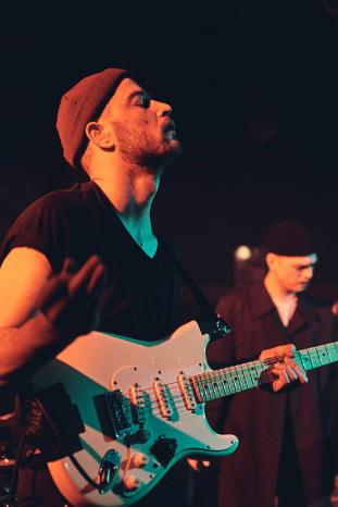 Mann mit Mütze spielt vor dunklem Hintergrund Gitarre