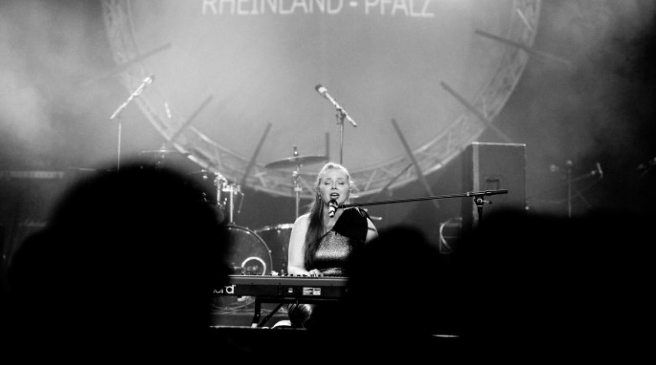 Eine Sängerin mit geschlossenen Augen sitzt am Klavier auf einer Bühne